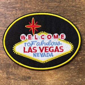 May include: Embroidered patch with a black oval background and a yellow border. The patch features the text "WELCOME TO Fabulous LAS VEGAS NEVADA" in red, white, and blue, along with a red star.