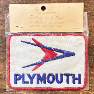 May include: A rectangular patch with a red border and the word "PLYMOUTH" in blue letters. The patch features a red and blue arrow design on a white background. The patch is packaged in a clear plastic bag.