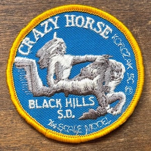 Könnte beinhalten: Eine weiße Keramik-Tasse mit schwarzem Henkel und dem Text "But First, Coffee" in fetter, schwarzer Schrift. Die Tasse steht vor einem verschwommenen Hintergrund. Die Tasse ist etwa 10 cm hoch.