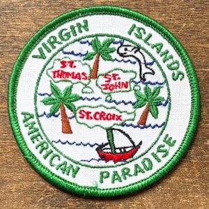 Puede incluir: Parche circular con un mapa de las Islas Vírgenes, palmeras, un velero y un delfín. El parche es blanco con borde verde y el texto "Virgin Islands American Paradise".