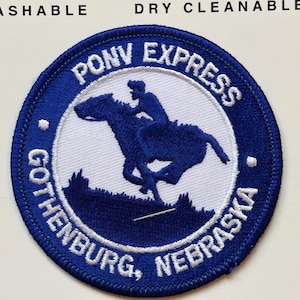 Puede incluir: Parche bordado azul y blanco con el texto "Pony Express Gothenburg, Nebraska" y una silueta de un jinete a caballo.