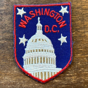 May include: Embroidered patch featuring the U.S. Capitol building in white and gold, with the text "WASHINGTON D.C." in red. The patch has a blue background with white star accents and a red border.