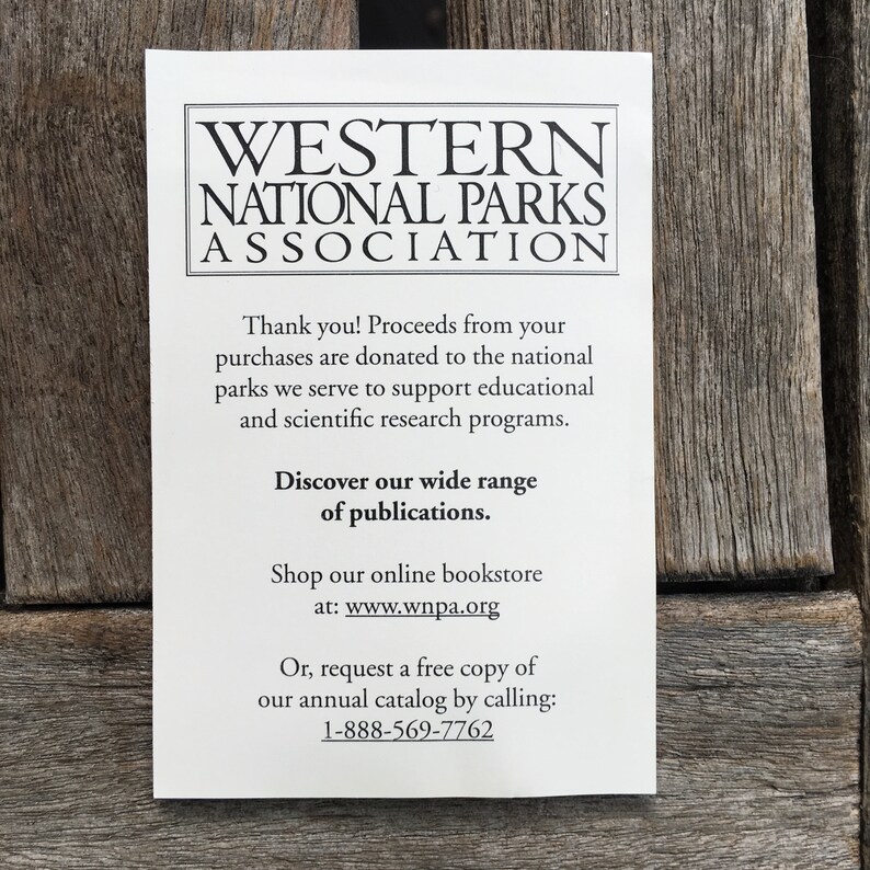 Op de afbeelding: Een witte kaart met zwarte tekst die reclame maakt voor de Western National Parks Association. De kaart legt uit dat de opbrengst van aankopen wordt gedoneerd om educatieve en wetenschappelijke onderzoeksprogramma's te ondersteunen. Het moedigt bezoekers ook aan om hun brede scala aan publicaties te ontdekken, in hun online boekhandel te winkelen of een gratis exemplaar van hun jaarlijkse catalogus aan te vragen door te bellen naar 1-888-569-7762.