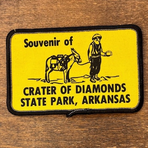 May include: Yellow souvenir patch with a black border. It features a miner, a donkey, and the text "Souvenir of Crater of Diamonds State Park, Arkansas". The patch is rectangular.