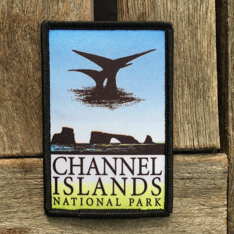 Op de afbeelding: Een geborduurde zwarte en witte patch met een blauwe en witte achtergrond. De patch toont een silhouet van een rotsformatie met een boog en de tekst "CHANNEL ISLANDS NATIONAL PARK".