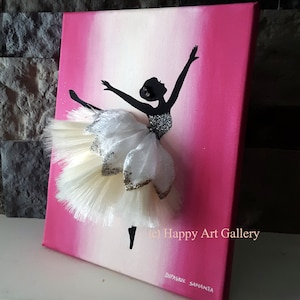 May include: A pink and white ombre canvas painting of a ballerina silhouette with a white tulle tutu. The tutu is embellished with gold glitter and white feathers. The painting is signed "Happy Art Gallery" and "Dyvasree Samanta".
