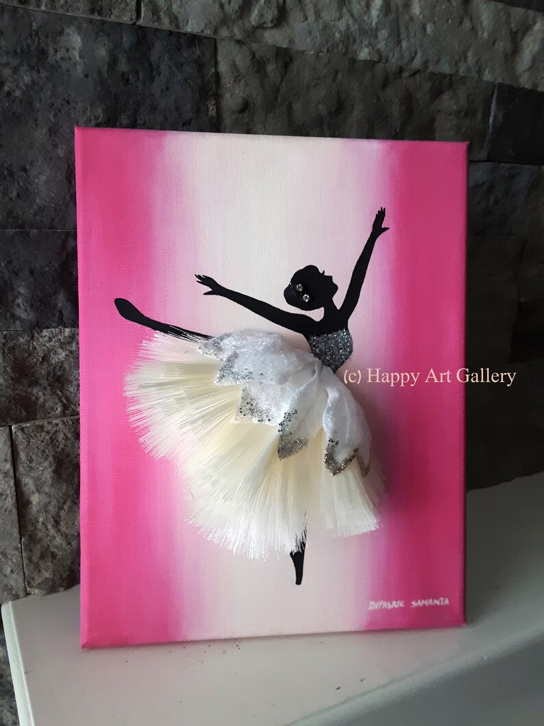 May include: A pink and white ombre canvas painting of a ballerina silhouette with a white and silver tutu. The tutu is made of fabric and has a 3D effect. The painting is signed "Diyasri Samantha" and includes the text "(c) Happy Art Gallery".