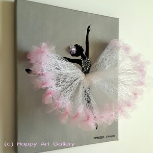 May include: A gray canvas with a black silhouette of a ballerina with a pink tulle tutu. The tutu is made of layered tulle with pink accents. The ballerina has a small purple flower on her head. The canvas is signed "Dipsaree Samantha" in the bottom right corner and "(c) Happy Art Gallery" in the bottom left corner.
