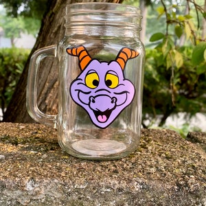 May include: A clear glass mason jar mug with a handle. The mug has a purple and orange cartoon dragon face decal on the front.