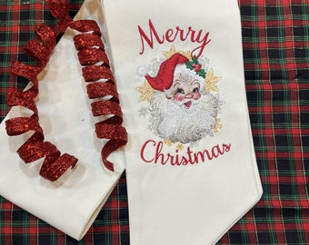 May include: White fabric with red embroidered text "Merry Christmas" and a vintage Santa Claus illustration.