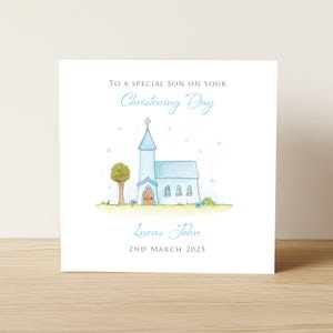 Op de afbeelding: Een vierkante wenskaart met een witte achtergrond en een aquarelillustratie van een lichtblauwe kerk met een toren en een boom. De tekst luidt: TO A SPECIAL SON ON YOUR Christening Day, Lucas John, 2ND MARCH 2025 in blauw en grijs.
