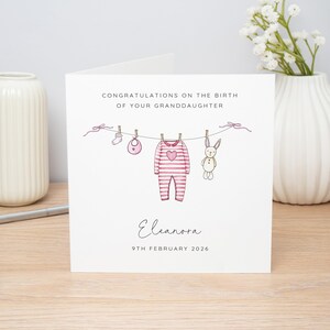 May include: A white greeting card with the text "CONGRATULATIONS ON THE BIRTH OF YOUR GRANDDAUGHTER". The card features a clothesline with baby clothes and a bunny illustration. The name "Eleanora" and the date "9TH FEBRUARY 2026" are also included.