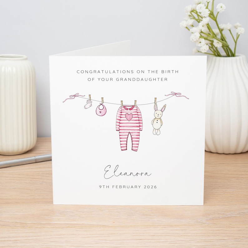 May include: A white greeting card with the text "CONGRATULATIONS ON THE BIRTH OF YOUR GRANDDAUGHTER". The card features a clothesline with baby clothes and a bunny illustration. The name "Eleanora" and the date "9TH FEBRUARY 2026" are also included.