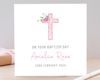 May include: A pink cross with white hearts on it, decorated with flowers. The text "On your Baptism Day Amelia Rose 23rd February 2025" is below the cross.