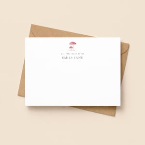 May include: A white rectangular stationery card with a brown envelope. The card features a small watercolour illustration of two red mushrooms at the top, with the text a little note from EMILY JANE printed in black ink below the mushrooms.