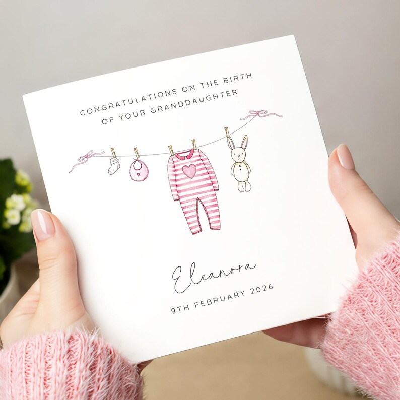 May include: A greeting card with the text "CONGRATULATIONS ON THE BIRTH OF YOUR GRANDDAUGHTER". The card features a clothesline with a baby onesie, bib, sock, and a stuffed bunny. The name "Eleanora" and the date "9TH FEBRUARY 2026" are also printed on the card.
