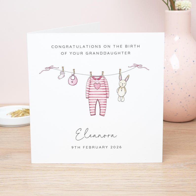 May include: A greeting card with the text "CONGRATULATIONS ON THE BIRTH OF YOUR GRANDDAUGHTER". The card features a clothesline with baby items: a onesie, bib, sock, and a stuffed bunny. The name "Eleanora" and the date "9TH FEBRUARY 2026" are also printed.
