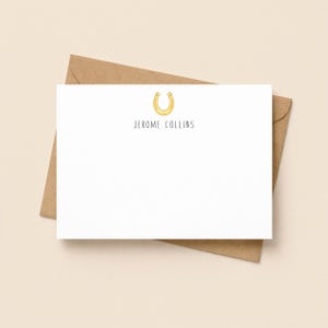May include: A white rectangular stationery card featuring a yellow horseshoe illustration centred at the top, with the name JEROME COLLINS printed in black sans-serif capital letters underneath, resting on a brown kraft paper envelope.