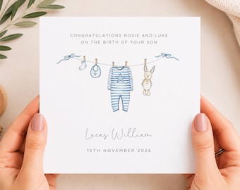 May include: A square white greeting card featuring a watercolor illustration of a clothesline with a blue striped onesie, a bib, a sock, and a stuffed rabbit. The text reads: CONGRATULATIONS ROSIE AND LUKE ON THE BIRTH OF YOUR SON, Lucas William, 15TH NOVEMBER 2026.