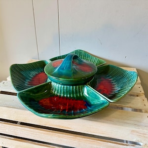 May include: A ceramic serving dish featuring four separate wedge-shaped compartments surrounding a central lidded bowl. The piece has a glossy finish with a deep green base color, textured ribbed details, and vibrant red accents in the center.