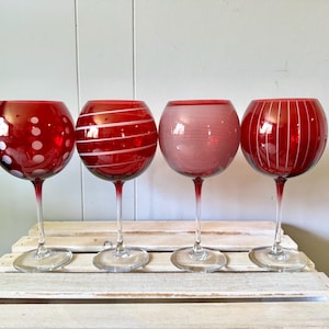May include: A set of four red glass goblets with clear stems and bases. Each goblet features a distinct white pattern: one with polka dots, one with diagonal stripes, one with fine horizontal lines, and one with vertical lines around the bowl.