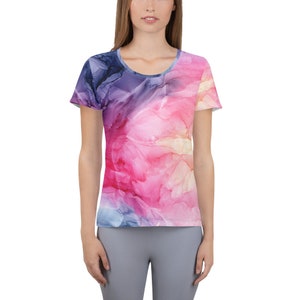 May include: A scoop-neck t-shirt with a vibrant, abstract watercolor design. The shirt features a blend of pink, purple, blue, and yellow hues, creating a flowing, artistic pattern. The short-sleeved top is made of a soft, comfortable material.