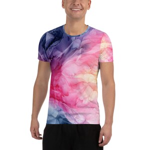 May include: A short-sleeved t-shirt with a vibrant, abstract design. The shirt features a blend of colors, including pink, purple, blue, and white, creating a watercolor-like effect. The shirt is a crew neck style and appears to be made of a soft, comfortable material.