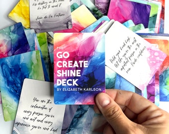 Może przedstawiać: Talia inspirujących kart z kolorowymi abstrakcyjnymi wzorami. Centralna karta głosi "The Go Create Shine Deck by Elizabeth Karlson". Inne karty zawierają cytaty i tła w stylu akwareli w odcieniach niebieskiego, fioletowego, różowego i żółtego.