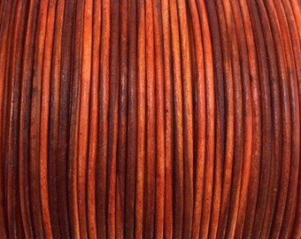 May include: Close-up of a spool of orange and brown leather cord. The cord is tightly wound and has a smooth, polished finish.