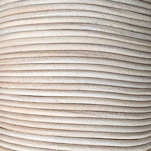 Op de afbeelding: Een close-up van een spoel met crèmekleurige lederen koord. Het koord is strak gewikkeld en heeft een glad, licht getextureerd oppervlak.