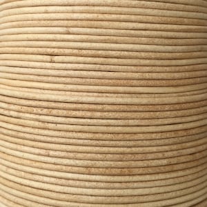 Op de afbeelding: Close-up van een spoel beige lederen koord. Het koord is strak gewikkeld en heeft een glad, licht getextureerd oppervlak.