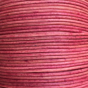 May include: Close-up of a reel of pink leather cord. The cord is wound tightly and has a smooth, slightly textured surface.