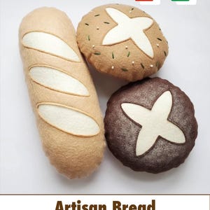 Puede incluir: Tres panes artesanales de fieltro: una baguette y dos panes redondos. La baguette es de color marrón claro con detalles blancos. Los panes redondos son marrones y tostados, con diseños blancos en forma de cruz. El texto dice "Artisan Bread DIGITAL DOWNLOAD."