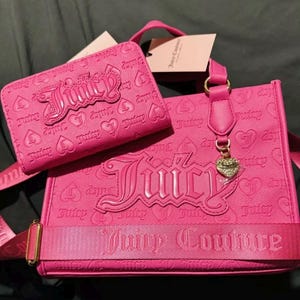 May include: A pink Juicy Couture handbag with a matching pink wallet. The handbag has a large "Juicy" logo and a gold heart charm. The wallet has a smaller "Juicy" logo.