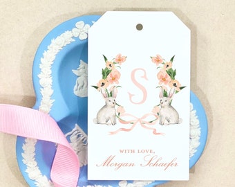 May include: A white gift tag with a pink floral wreath and two white bunnies. The letter "S" is in the center of the wreath. The text "With love, Morgan Schaefer" is at the bottom of the tag.