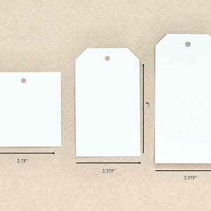 K&ouml;nnte beinhalten: Drei wei&szlig;e Geschenkanh&auml;nger in verschiedenen Gr&ouml;&szlig;en. Der gr&ouml;&szlig;te Anh&auml;nger ist 12,1 cm hoch und 6 cm breit. Der mittlere Anh&auml;nger ist 10,2 cm hoch und 6 cm breit. Der kleinste Anh&auml;nger ist 7 cm breit und 7 cm hoch.