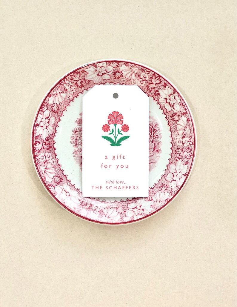 K&ouml;nnte beinhalten: Ein wei&szlig;er Geschenkanh&auml;nger mit einer roten Blumenillustration und dem Text "a gift for you with love, THE SCHAEFERS".