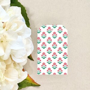 K&ouml;nnte beinhalten: Ein wei&szlig;er Geschenkanh&auml;nger mit einem sich wiederholenden Muster aus rosa Blumen und gr&uuml;nen Bl&auml;ttern.