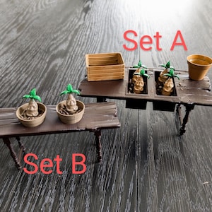 Puede incluir: Dos juegos de plantas en maceta, un juego con cuatro plantas y el otro con dos plantas. Las plantas son marrones y tienen hojas verdes. Los juegos están sobre mesas de madera con las palabras "Set A" y "Set B" escritas en ellas.