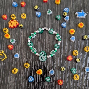 May include: A green and white beaded bracelet with a green snake charm. The bracelet is surrounded by small green, blue, yellow, and red shields.