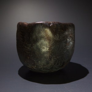 May include: A dark brown ceramic bowl with a textured surface and a metallic sheen. The bowl has a rounded shape and a slightly flared rim.