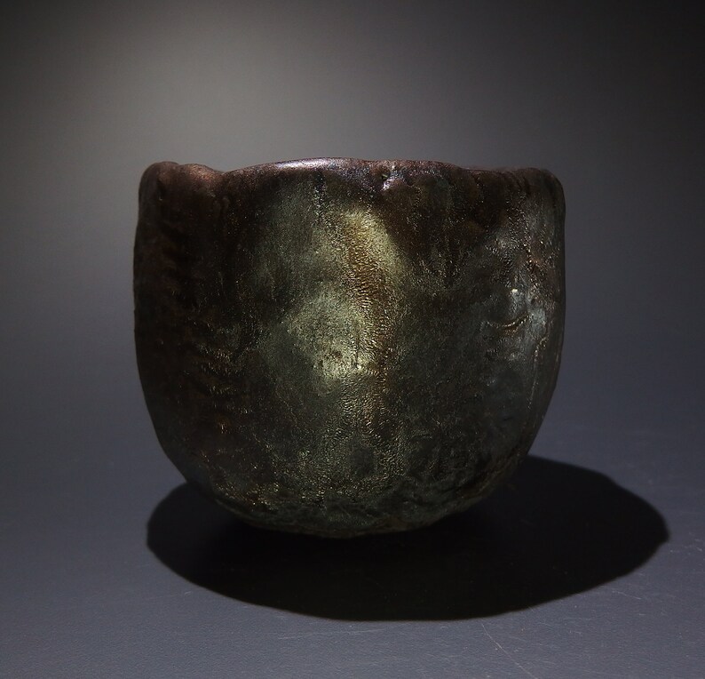 May include: A dark brown ceramic bowl with a textured surface and a metallic sheen. The bowl has a rounded shape and a slightly flared rim.