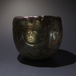 May include: A dark gray ceramic bowl with a textured surface and a metallic sheen. The bowl has a rounded shape and a wide opening.