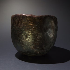 May include: A dark brown ceramic bowl with a textured, uneven surface. The bowl has a metallic sheen with hints of gold and green.