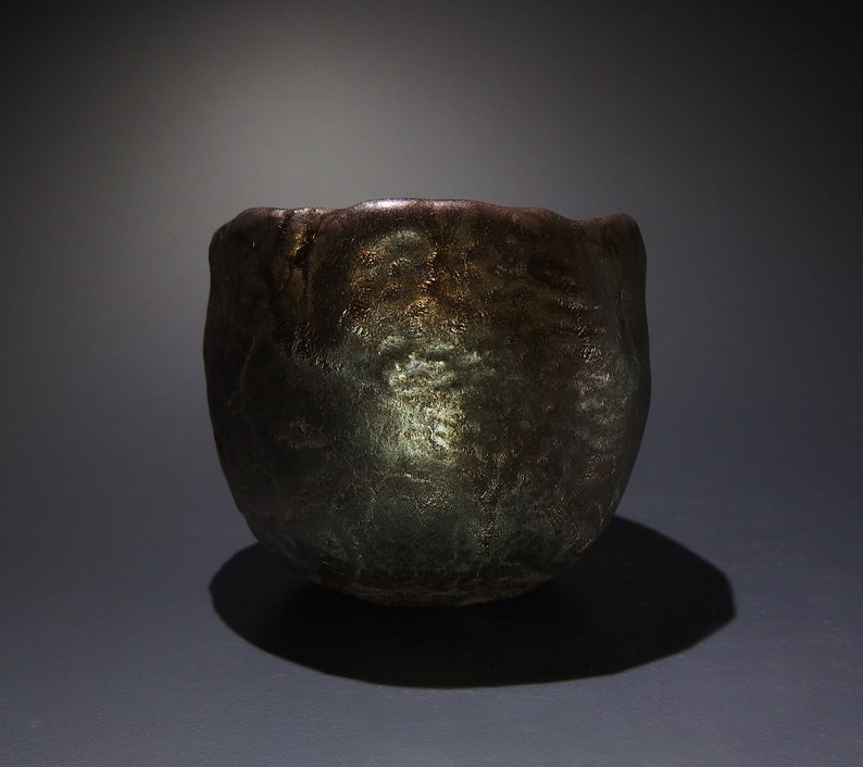 May include: A dark brown ceramic teacup with a textured surface and a metallic sheen.