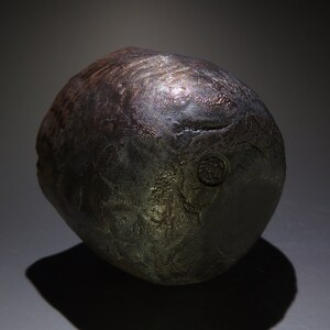 May include: A dark gray ceramic pot with a textured surface and a circular mark on the side.