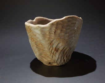 May include: A small, white ceramic bowl with a textured, organic surface. The bowl has a slightly irregular shape and a wide, open mouth.