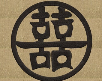 May include: Black embroidered Chinese character for "double happiness" in a circle on a beige fabric background.