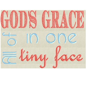 May include: Embroidered design with the text "God's Grace in one tiny face" in red and blue thread on a beige fabric background.
