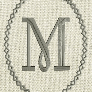 May include: A gray embroidered letter M in a decorative gray frame on a beige linen background.